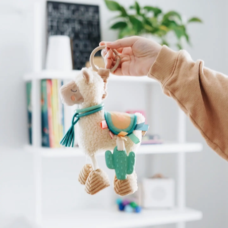 Hand holding a plush llama toy with a cactus design against a blurred indoor background