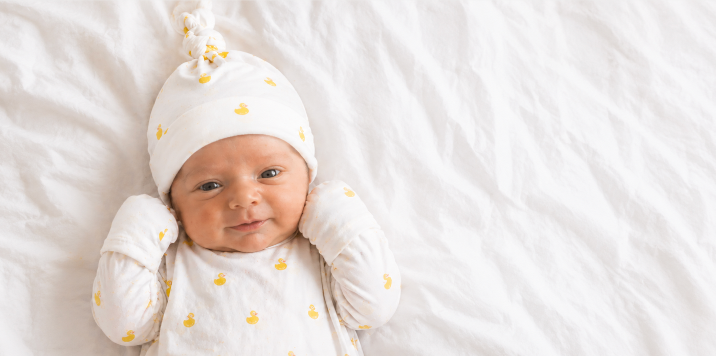 Newborn baby wearing a white pima cotton soft hat with yellow polka dots on a white blanket