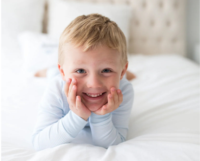 Smiling boy lying on bed in blue pajamas.
