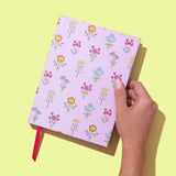 Hand holding a notebook with floral pattern on a yellow background