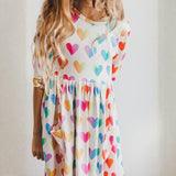 Child wearing a dress with colorful heart pattern against a plain background