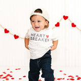 Child wearing a 'Heart Breaker' shirt with red heart decorations in the background