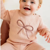 Baby wearing a pink knitted outfit with a bow design on a white background
