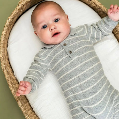 Baby in a striped outfit lying on a white cushion inside a wicker basket.