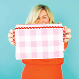 Person holding a pink and white checkered pouch with red trim against a blue background