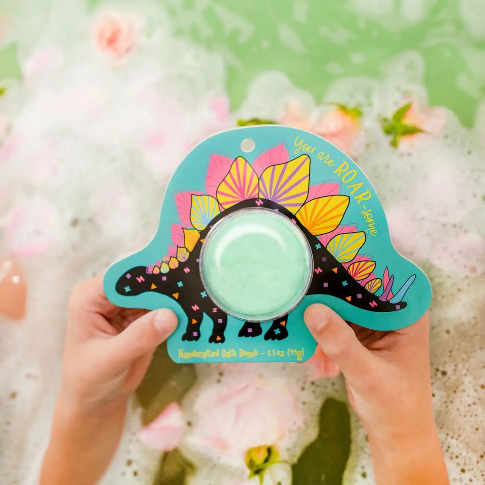 Colorful dinosaur-shaped bath bomb with a green center held by hands against a floral background.