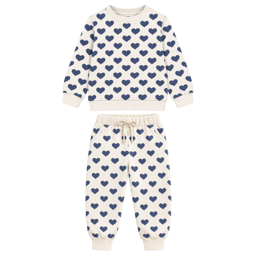A two-piece children's sweatshirt and jogger pants set in cream with a repeating navy blue heart pattern, displayed on a solid white background.