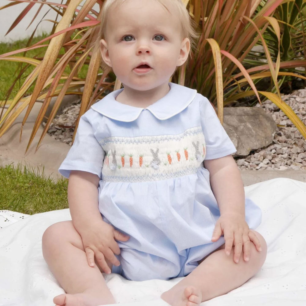 Bunny Smocked Babysuit in Blue a baby boy sitting on a floor