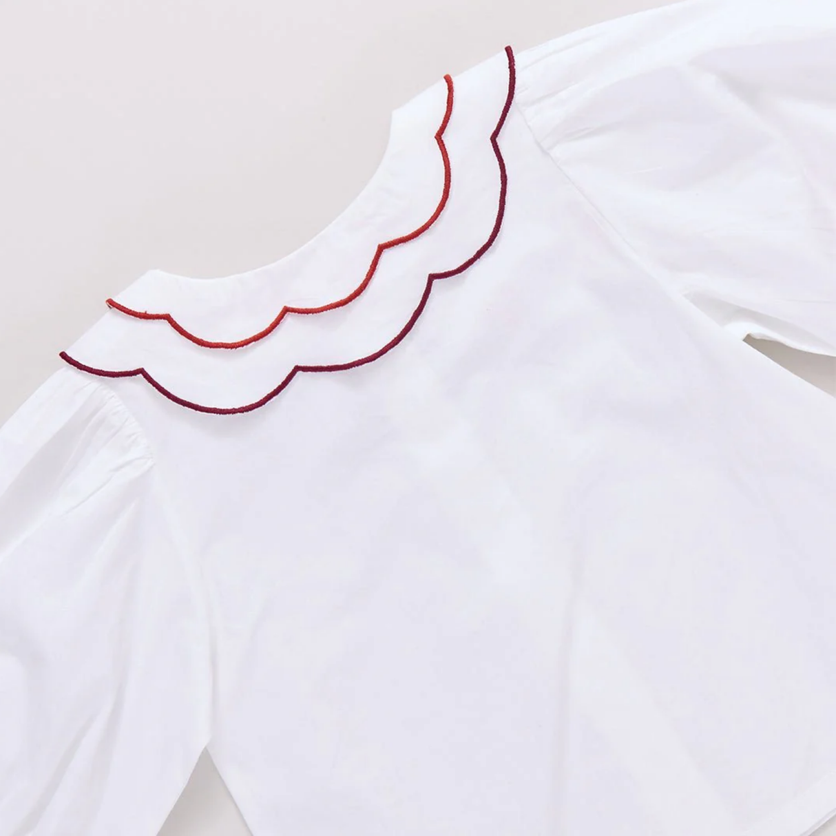 White garment with red scalloped trim on a light background