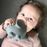 Baby holding a gray elephant-shaped object against a textured surface