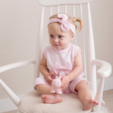 Baby in pink outfit sitting on a white rocking chair holding a pink toy.