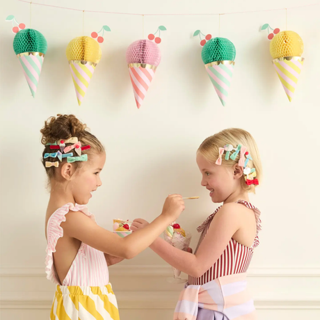 Two young girls in colorful outfits interacting with ice cream-themed decorations on a wall.