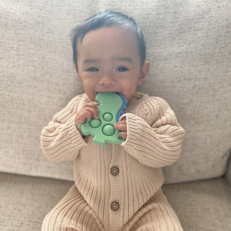 a baby biting the Dino Itzy Pop Sensory Popper Toy in Green