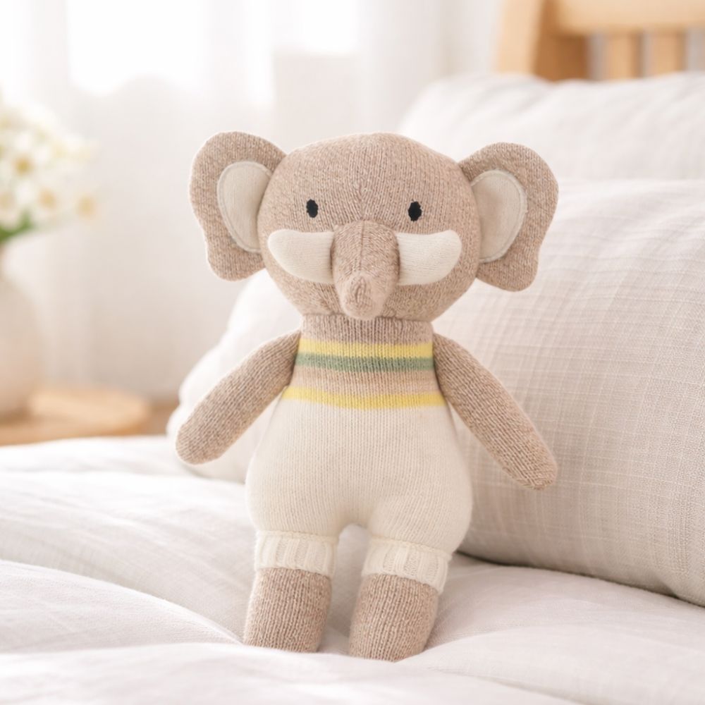 Plush elephant toy with a striped sweater on a soft surface