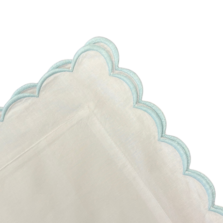 Close-up of a scalloped edge pillow with light blue trim on a white background