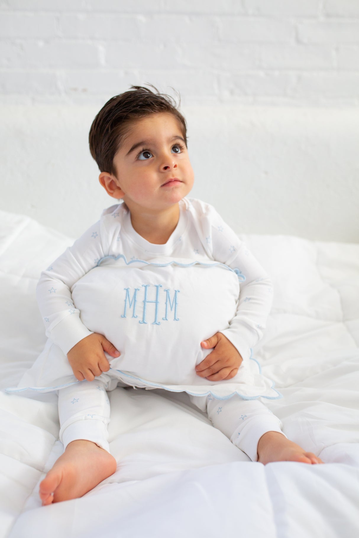 Child holding a pillow with 'MHM' monogram on a white background