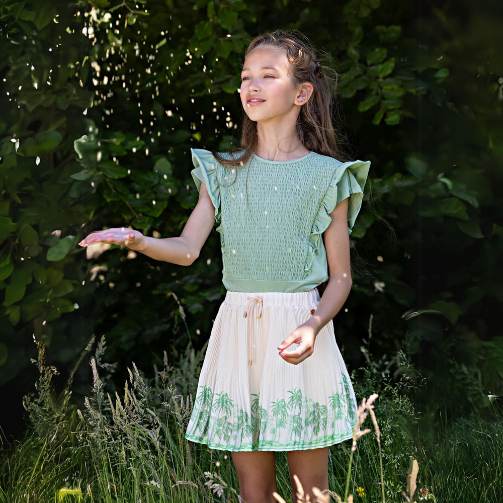 Nulan Palm Tree Pleated Skirt in Pearled Ivory a girl throwing flowers