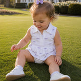 Child sitting on grass wearing a white outfit with purple dragonfly pattern - Pima RIley Romper