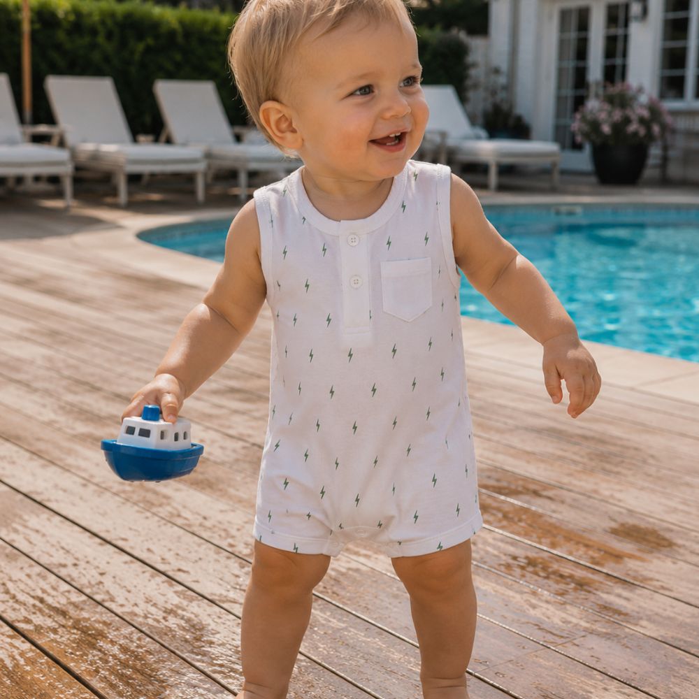 Child holding a toy boat on a wooden deck by a pool in Pima Romper