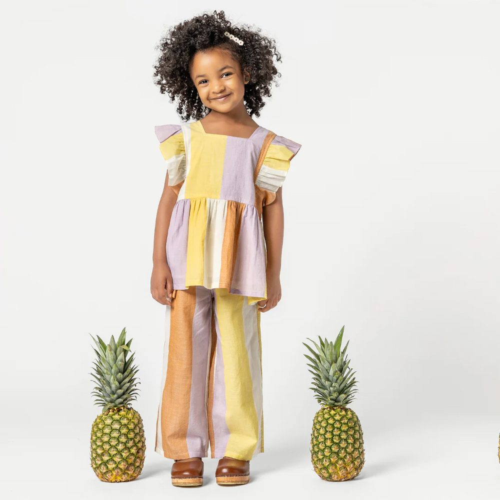a girl standing beside the pineapples wearing Elsie Top - Desert Stripe