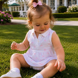 Child sitting on grass wearing a white dress with pink details