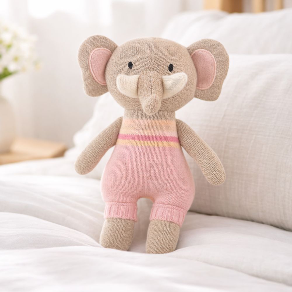 Knitted elephant toy in pink and beige outfit on a white surface