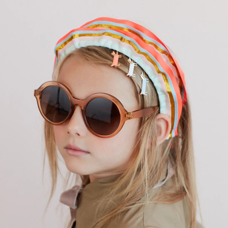 Young girl wearing colorful headband and sunglasses against a plain background
