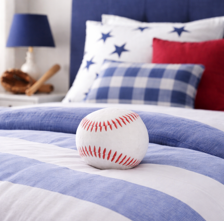 Baseball on a bed with blue and white striped bedding and decorative pillows.