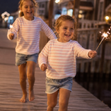 Two young girls running on a wooden dock holding sparklers at night.