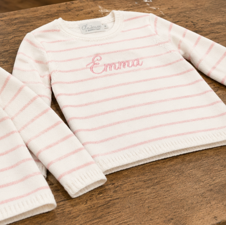White sweater with pink stripes and embroidered name on a wooden surface
