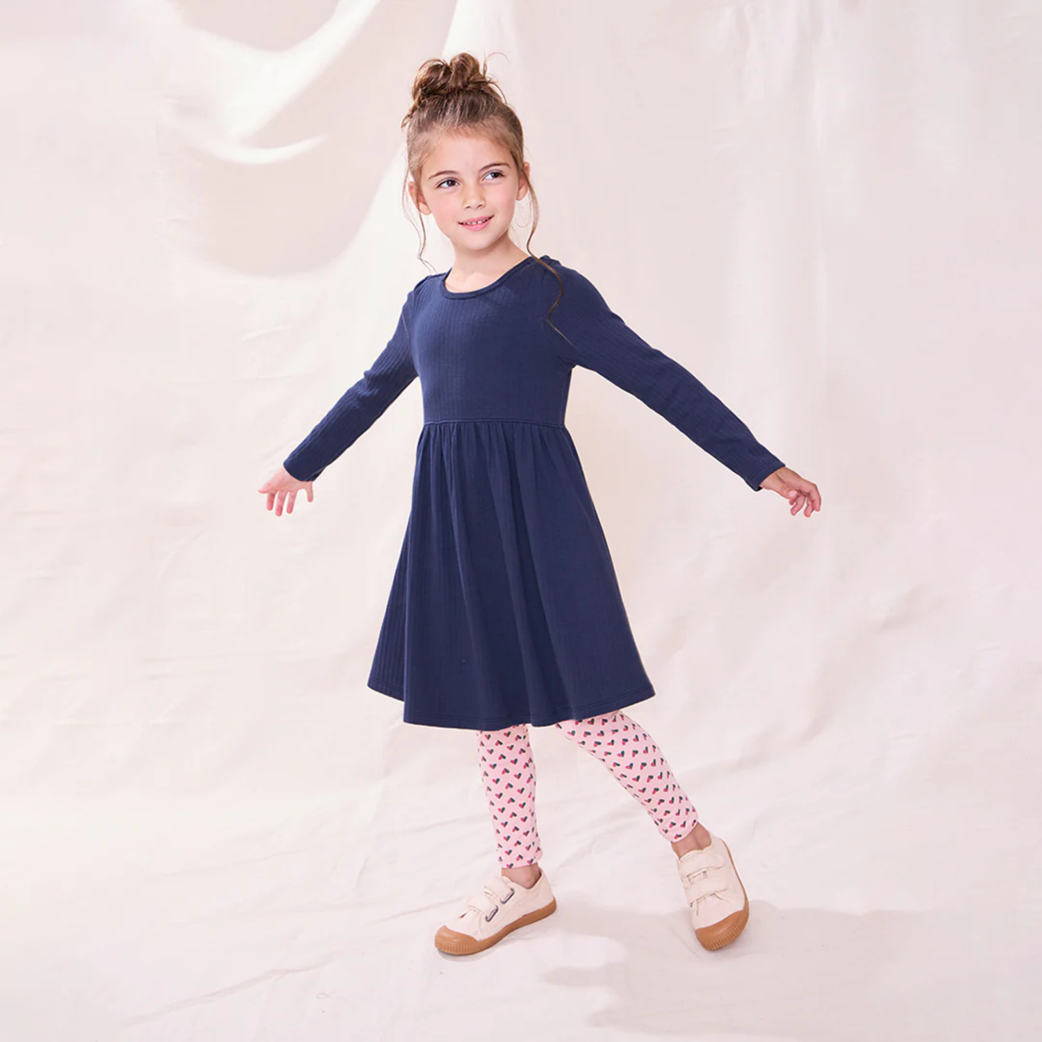 Young girl wearing a navy blue dress with pink patterned leggings on a white background