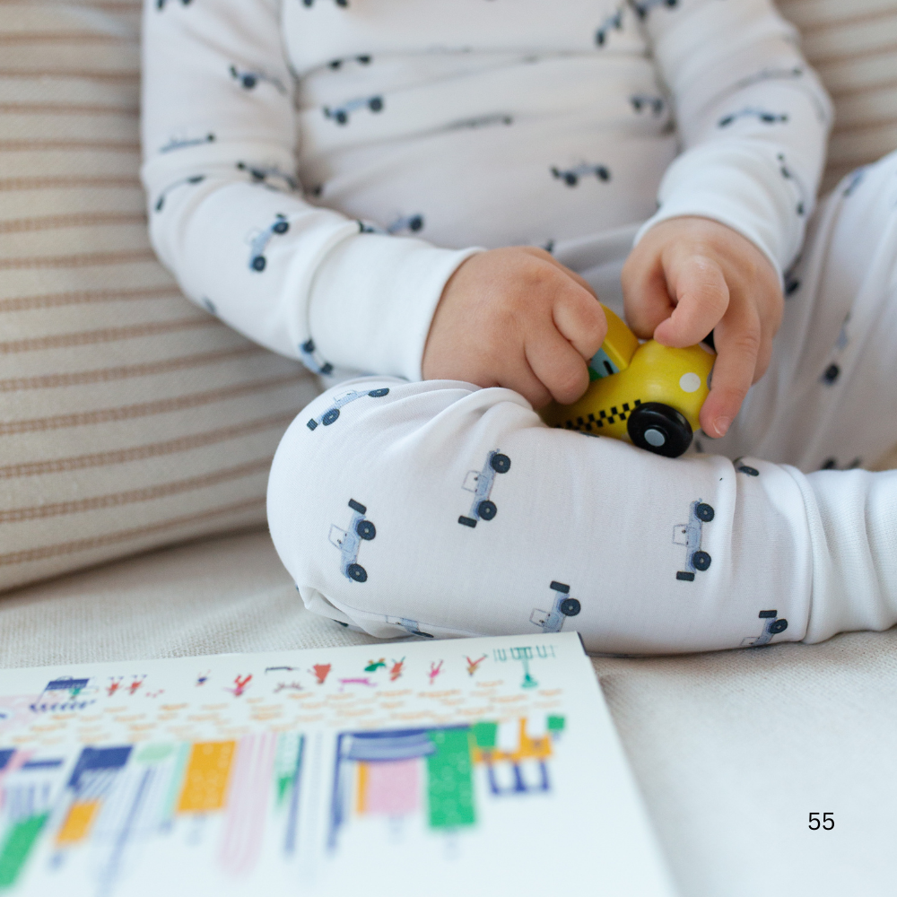 Child playing with a toy car on a couch next to a book