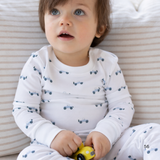 Child wearing a white onesie with blue car patterns, sitting on a striped surface.