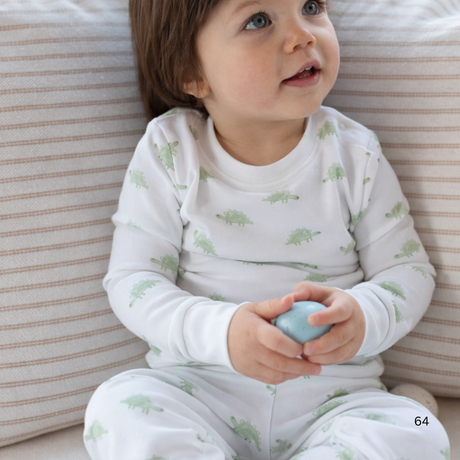 Child wearing a white onesie with green patterns, sitting on a striped surface.