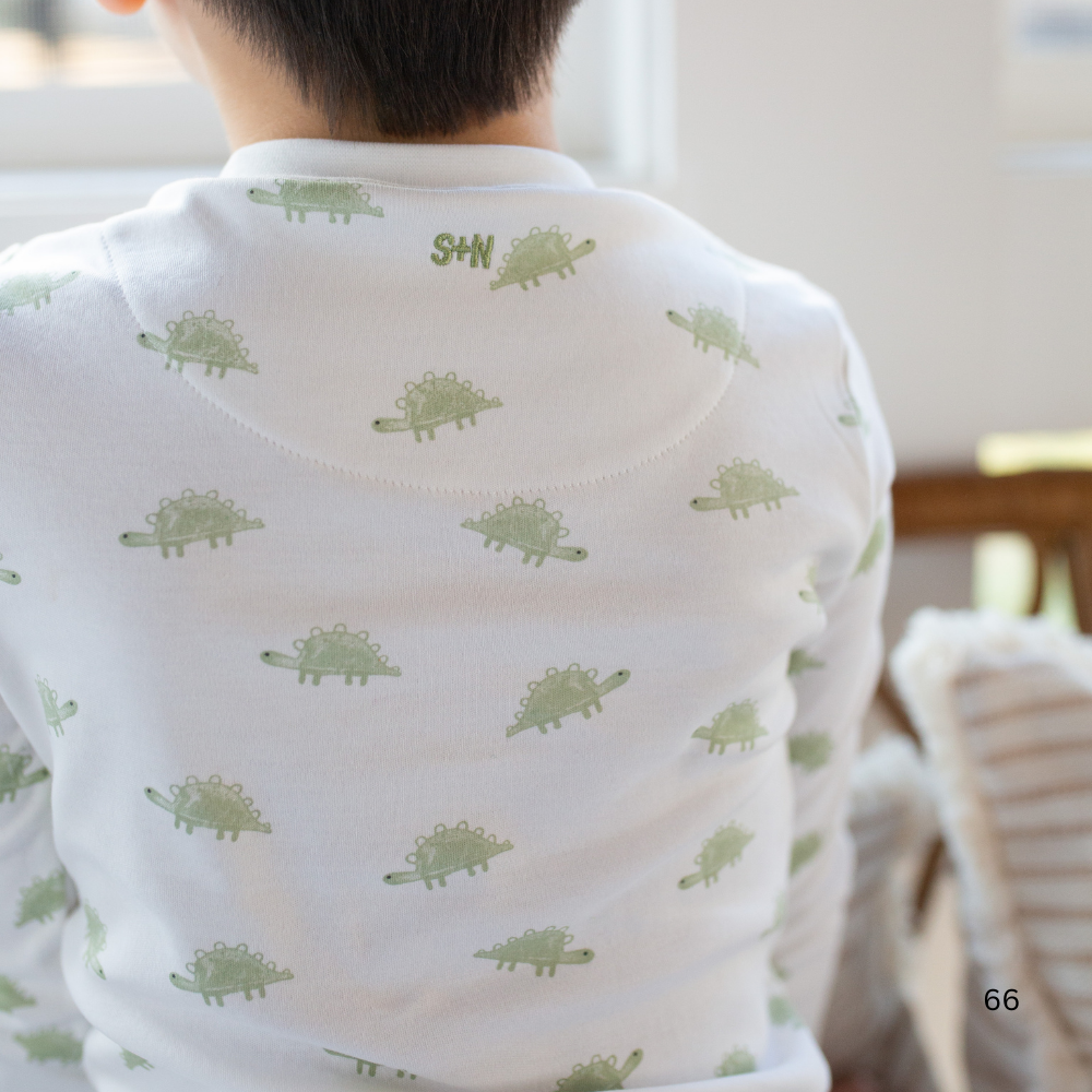 Person wearing a white shirt with green dinosaur patterns in a casual setting.