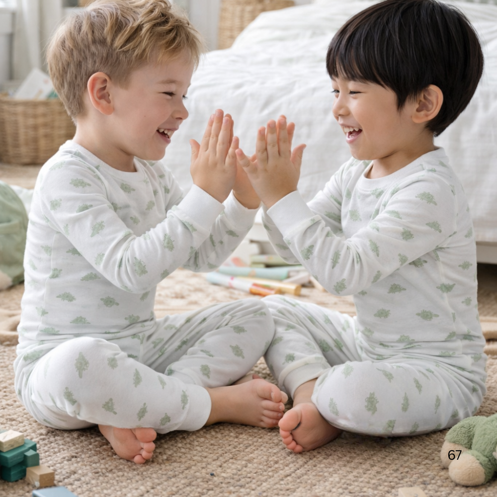 Two children in matching pajamas sitting on the floor and giving each other a high-five.