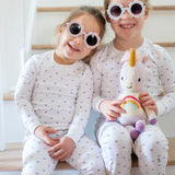 Two children in matching pajamas with a unicorn plush toy, sitting on a staircase.