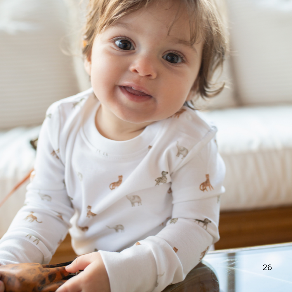 Baby wearing a white long-sleeve shirt with small patterns, sitting on a couch.