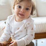 Baby wearing a white long-sleeve shirt with small patterns, sitting on a couch.