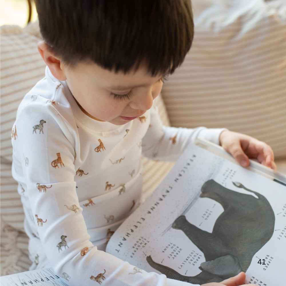 Child reading a book with animal illustrations on a soft surface