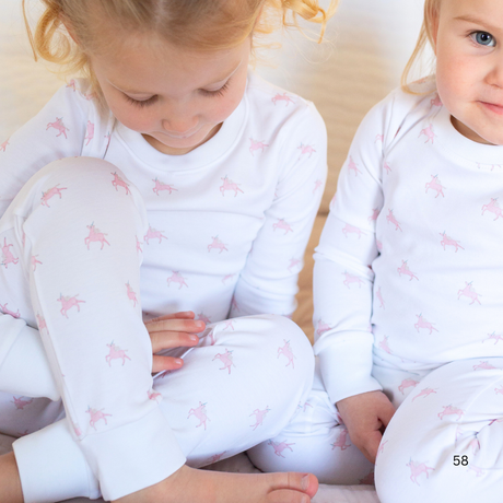 Two children wearing matching pajamas with a pink pattern on a beige background