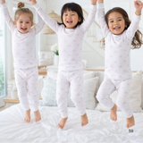 Three children in matching pajamas jumping on a bed in a bright room.