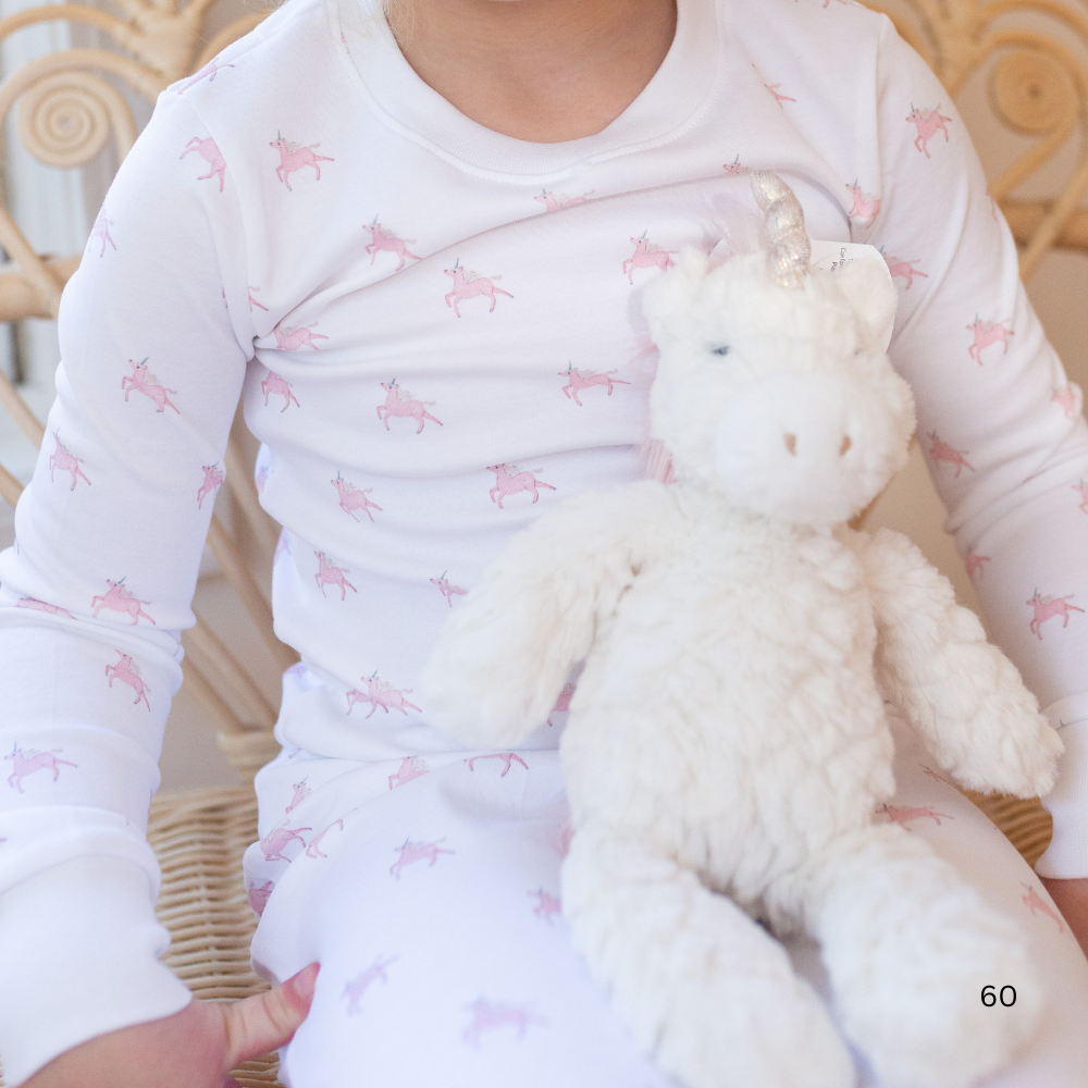 Child wearing a white onesie with pink patterns, holding a white unicorn.
